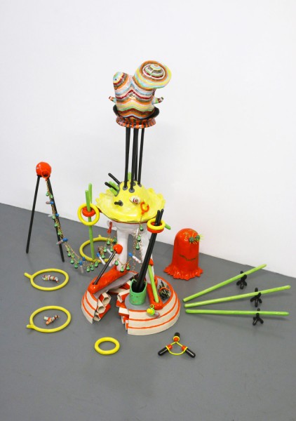 Installation view of a sculpture made of different colored pieces in green, yellow, ceramic objects installed on top of each other, on the floor