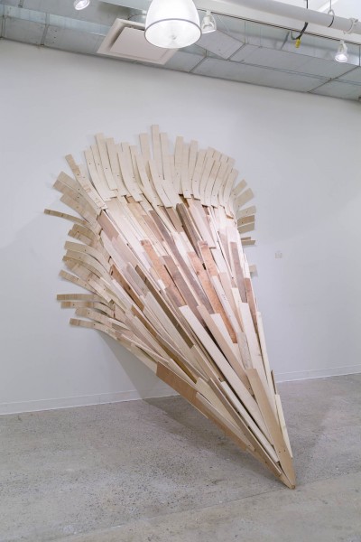 View of a wooden sculpture in a conic shape installed with nails on the wall.