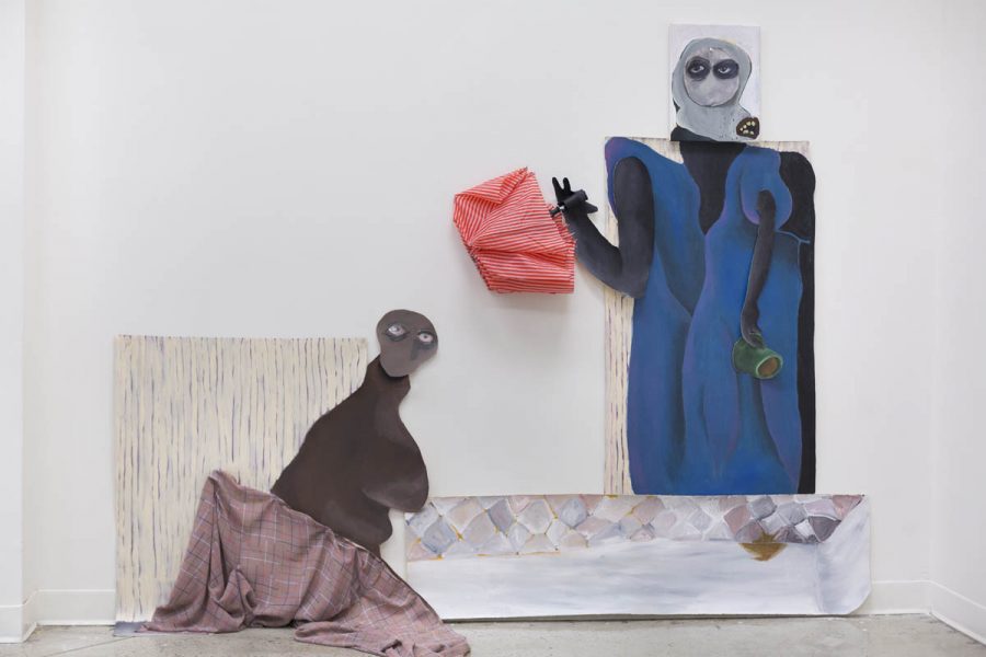 Installation view of a composite artwork with two silhouettes. The Standing one is made of pieces of canvas painted as the body dressed with a blue fabric, on the head, it has a white hood, in the right hand, it has a green object painted, and in the left hand, it has attached a real red closed umbrella. Bellow, it is a painting looking like a mattress. On the left side is another silhouette made of canvas painted in marron, and on the bottom part is covered with a brown piece of fabric. Behind it is a square backdrop with a vertical line of beige color. The artwork is installed on a wall