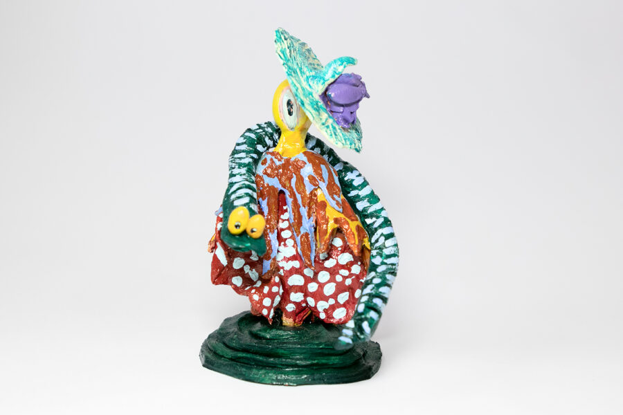 A small figurative ceramic sculpture brightly painted, featuring a yellow figure loosely clothed and wrapped with a cartoonish snake.