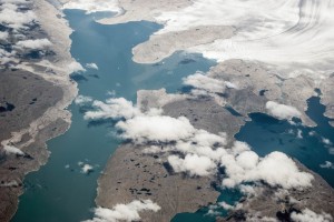 An aerial view of Greenland's landscape with water and ground and clouds covering parts of the landscape.