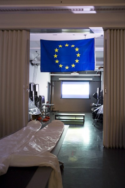  There is a multimedia installation view with a European Union flag, hazmat suit, and a video called 