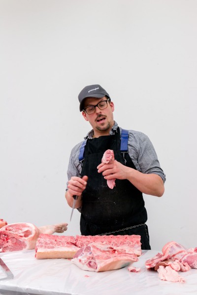 A person in front of the table with a knife in one hand and a piece of pork meat in the other hand and pork meat on the table.