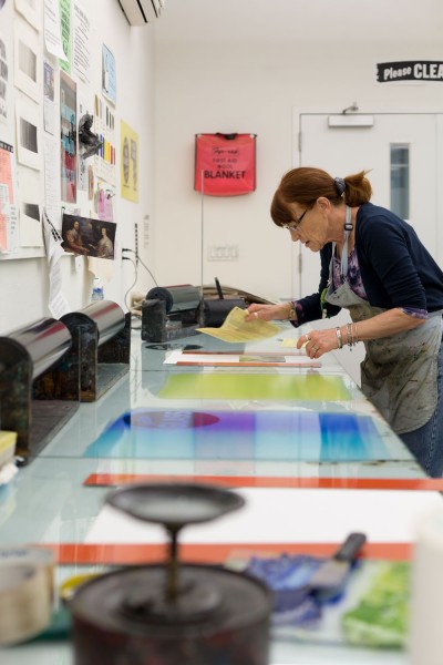 A student examining her etching plate. In the foreground, a color blend of different blues is rolled out onto the glass countertop.