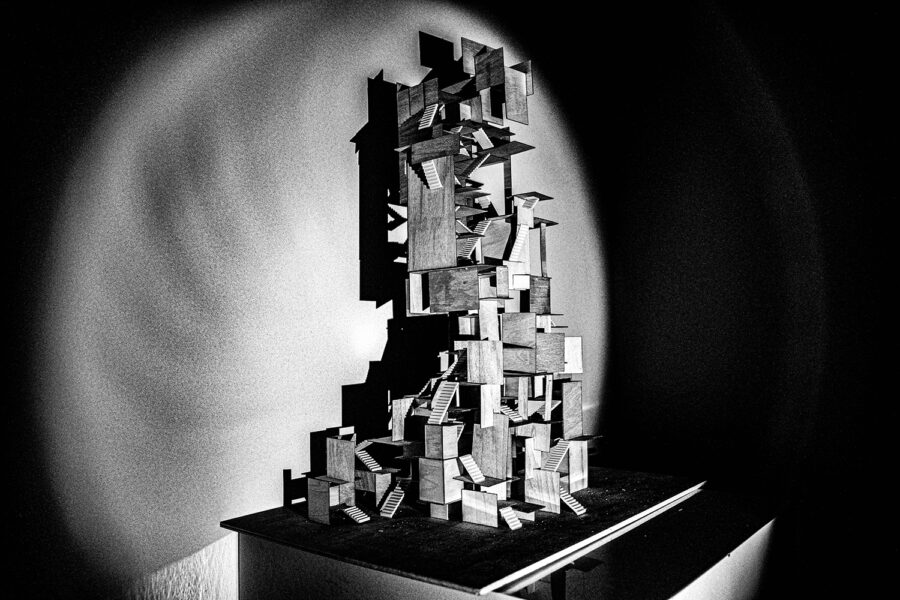 An assemblage of wooden blocks and platforms, suggesting a complex architectural model. Spot-lit and photographed in black and white.