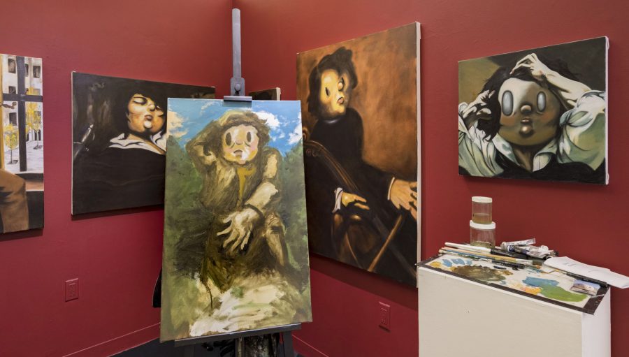 A photograph of S von Puttkammer's studio with several figurative paintings hanging on a red wall and a painting on an easel.