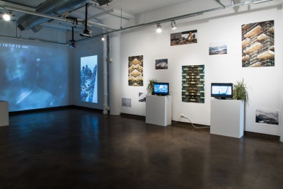 Installation view of image projections on the wall, tv screens with images on it, and prints installed on a white wall