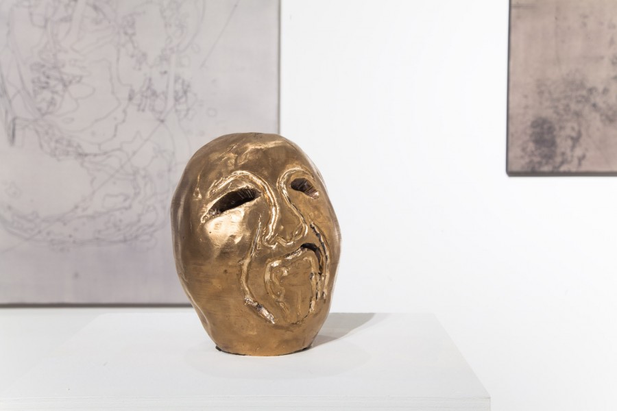 Humanoid head sculpture with a sad expression made of a shiny golden material
