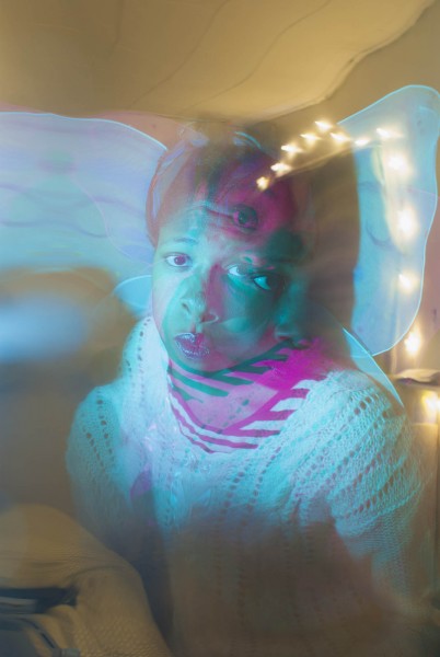 An ink-jet stereoscopic portrait print of a person with green light on their face and fairy lights in the background.