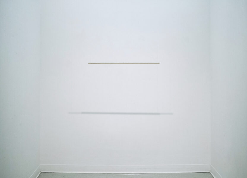 In a white gallery space there are two rectangular brass bars in the center near the rear wall. Identical in size, but slightly apart with height difference. Floating without any support.