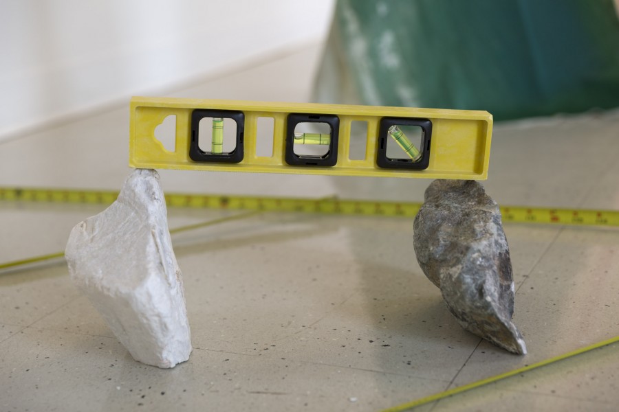 A white and a grey rock on the floor, a measuring roulette, and a leveler.