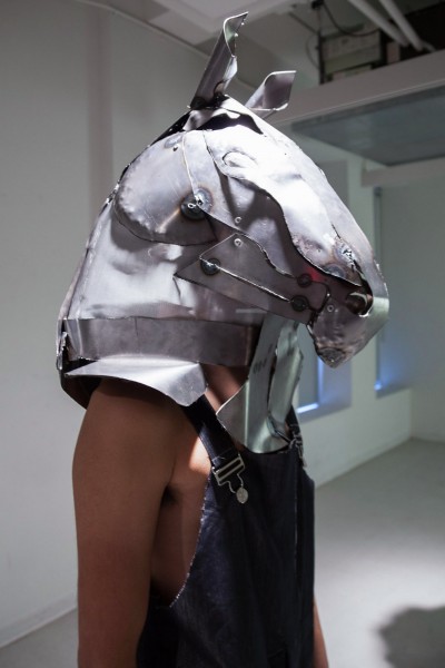 A person wearing a metal welded helmet in the shape of a horse head
