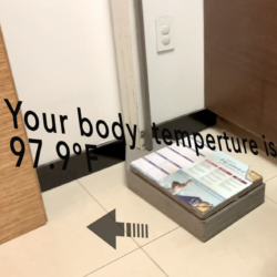 A video still showing wood-paneled surfaces, a tile floor, a power outlet on a white wall and a box-like shape topped with what may be a web page. Black text overlays the image with the words "Your body temperature is 97.9 degrees F."