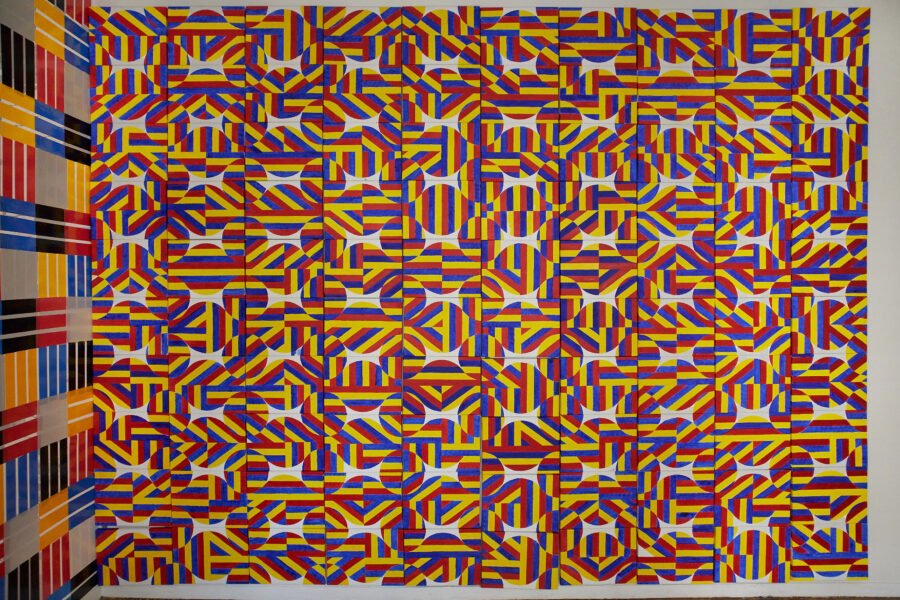 100 pieces of 12 x 9 inch canvas attached on the wall painted in colors of red, blue, and yellow stripes.