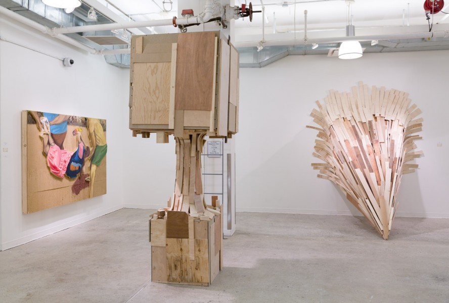 Installation view of wooden sculpture made in the form of a tower with a giant cube on top, a column and a smaller cube on the bottom part on the floor, a conic shaped-sculpture made of narrow wood pieces and another sculpture installed on the left side wall with different colored materials