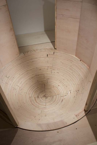 Inside view of a wooden sculpture with a round bottom made of thin wood pieces in round shapes and walls are made of wooden boards.