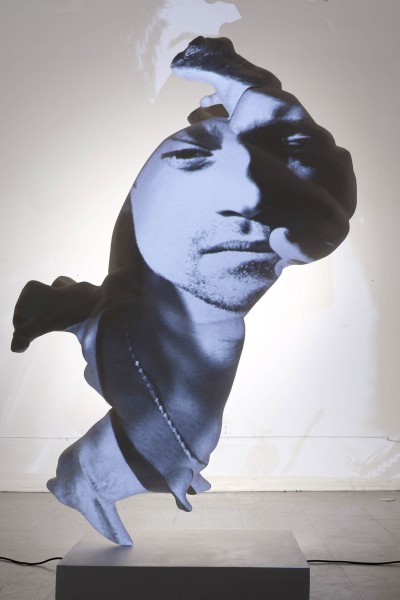 A blue and black portrait of a man is projected on the white rhino sculpture.