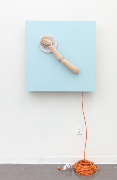 An artwork by Titus McBeath titled "Cain and Able (Able)" consisting of a light blue painting with a manikin arm holding a plate attached to it. A long orange extension cord is hanging from the back of the painting and is coiled up on the floor.