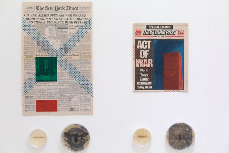 Installation of two newspaper pages, on the left, is a large one from The New Yorker and beside it is a smaller one still from The new yorker, but this illustrated the red building on a blue background, and the title Act of War World Trade Center destroyed: many dead. Under the newspaper pages are four round containers, two with a small piece of paper and a text, and the other one are housing a small insect.