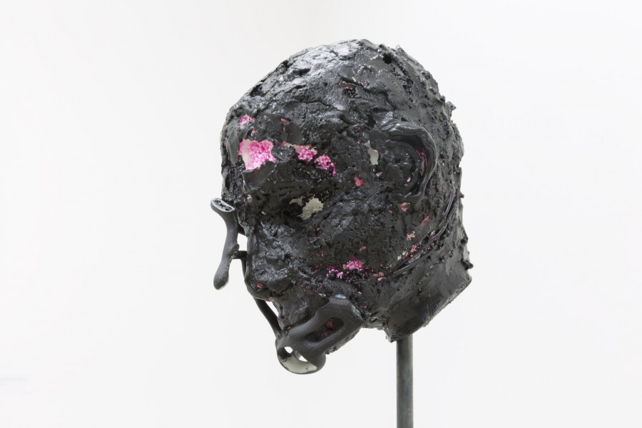 Sculpture of a head made of black materials with spots of small pink balls.