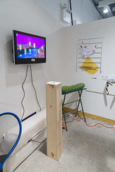 Installation view of a flat-screen tv with an image, wood stand with a button on top, and other media.