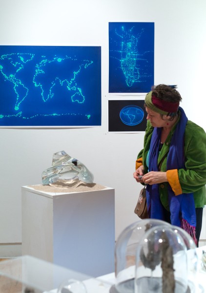 A person looks at an organic-shaped glass sculpture, and in the background are world map prints.