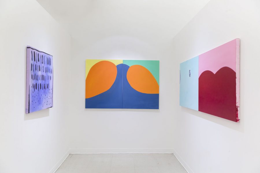 Three paintings installed, one on each wall from left to right the paintings are purple, black, the middle painting is blue with orange round shapes and a yellow and green background, the left has a painting that is half light blue, and half pink with a big red round shape