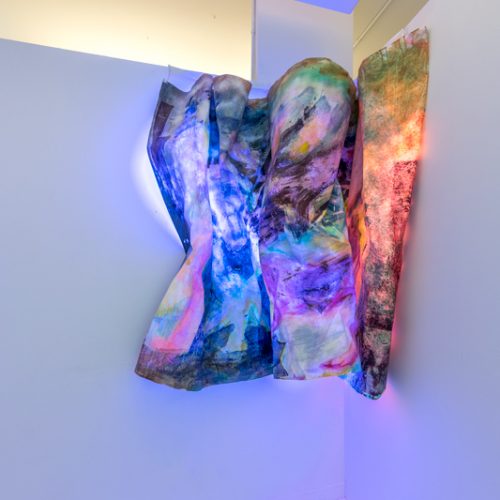 Installation view of artwork by Yesiyu Zhao. Chromatic mixed media artwork backlit by multicolored neon lights.