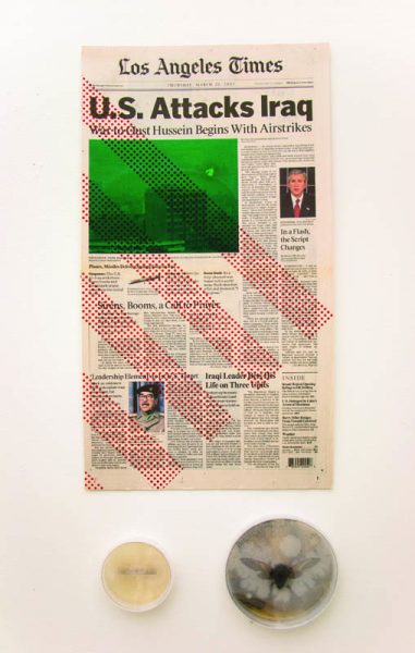 A page of Los Angeles Times with the title U.S. Attacks Iraq with a news material and Gorge Bush and Saddam Husein pictures beside the text. under the news page are two rounded containers, one with a yellow organic material and the other containing a preserved insect