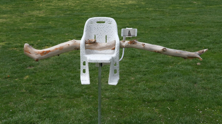 A mixed-media sculpture with a white mosaic tile covered chair and a large light colored branch inserted through the chair