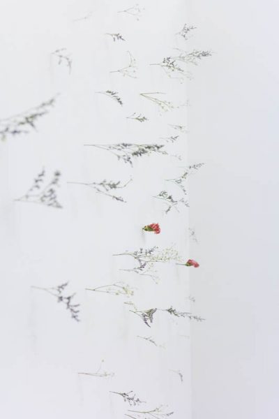 A side-view of pink flowers and thin white flowers inserted in a white wall