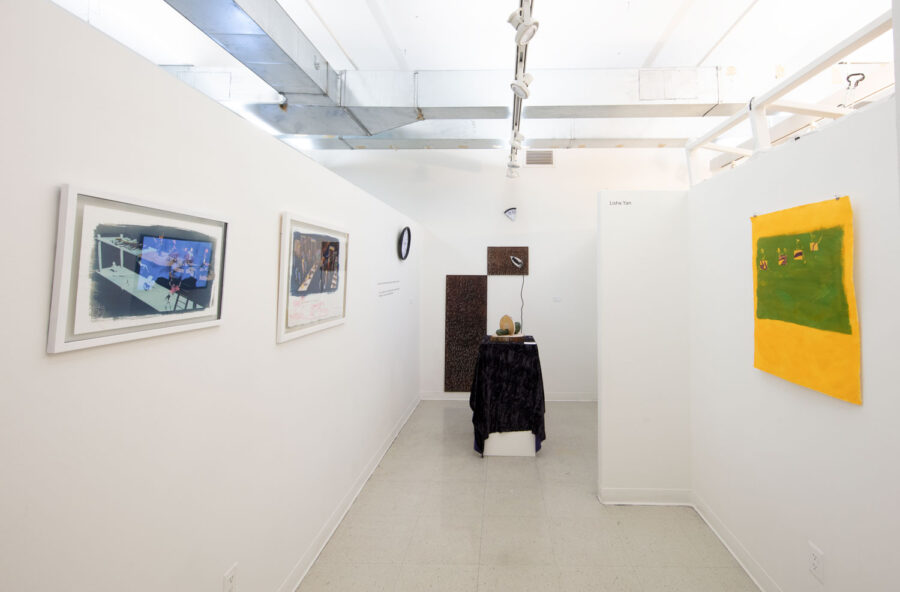 Huang's studio space. The walls are white and there are three pieces hanging on the left side wall. On the right is one painting hanging. In the center is a pedestal with a cloth draped over it.