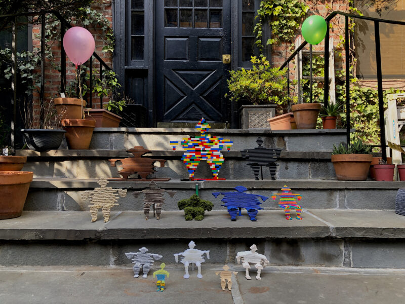 Installation shot on the steps of an apartment building with potted plants and small plastic figurines.