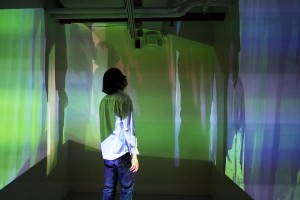 A person looks at image projections on all walls of the room