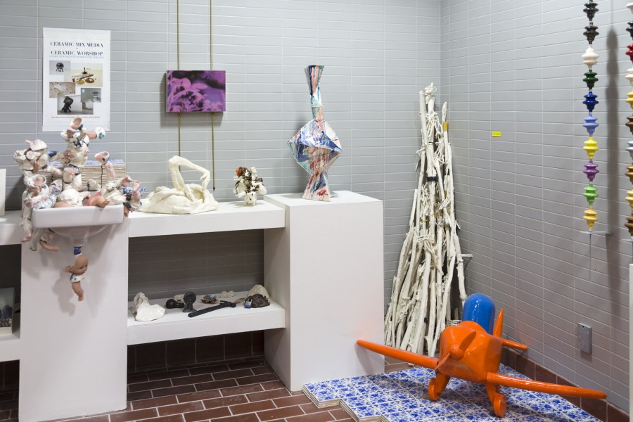 Installation view of ceramic sculptures, which include abstract shapes, geometric shapes, an orange plane, and white tree branches