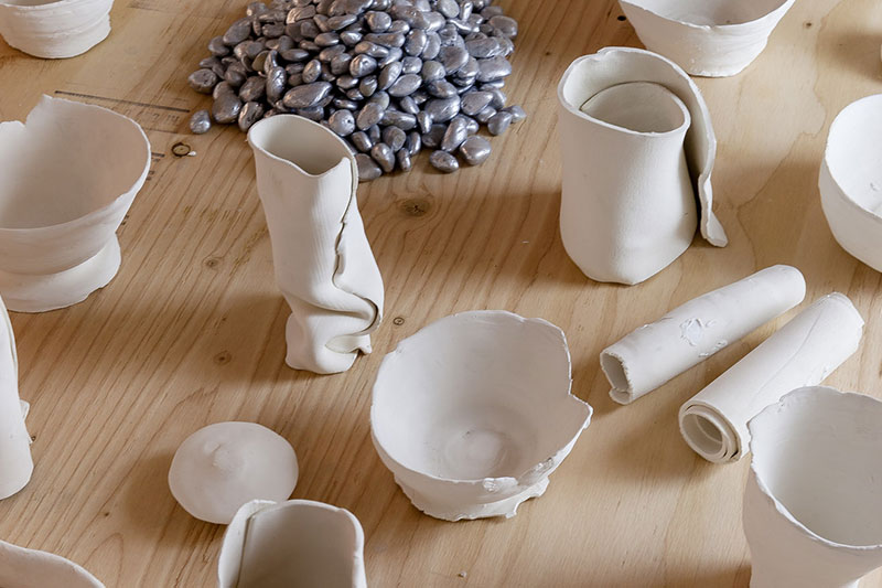 A closer look at ceramic sculptures of glasses and bowls, and at the top of the image, a pile of silver beans.