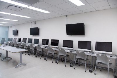 Overview of the computer lab with iMacs along the wall and on the left side of the frame is the teaching desk in the middle of the room