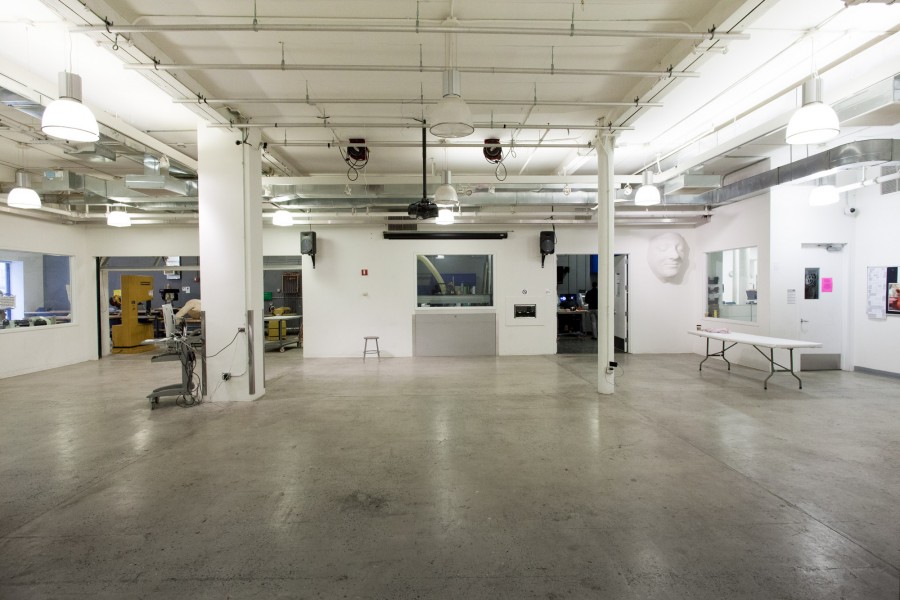 A photograph of the large main sculpture workspace of the BFA Fine Arts department at SVA. I large white-walled workspace with a polished concrete floor. The woodshed and CNC sculpture room are visible through open doors.
