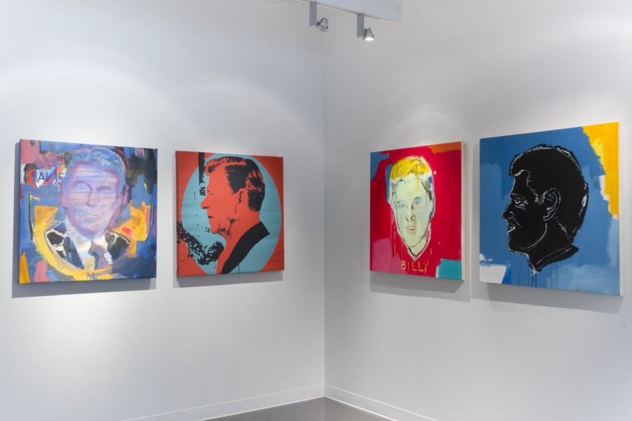 A corner of a gallery with four paintings hanging on the wall. The paintings are square and depict different US presidents on each painting with vibrant colors painted over them.
