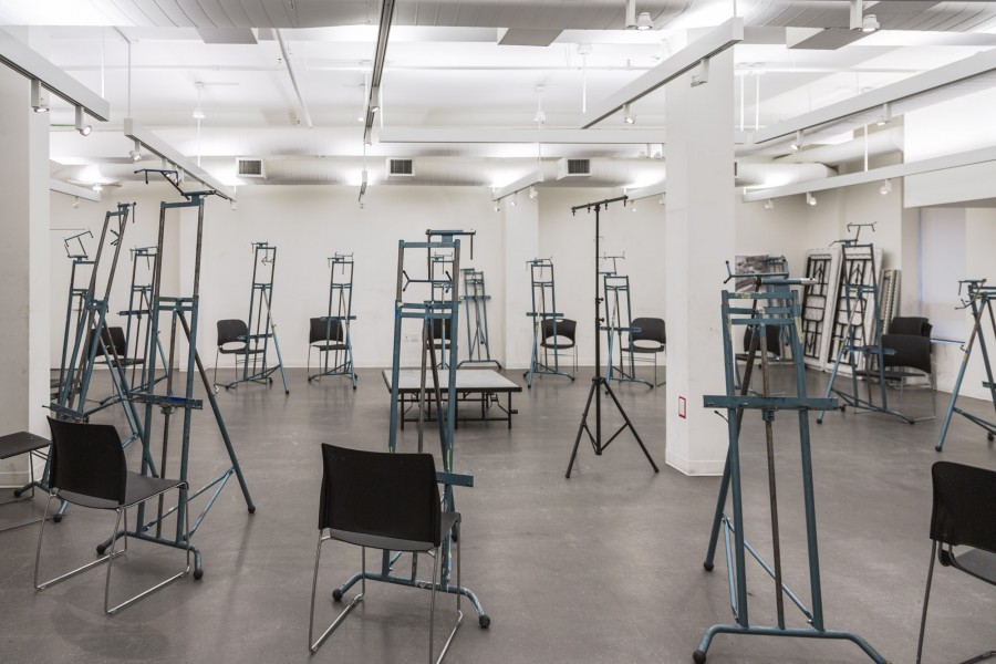 A drawing classroom at the BFA Fine Arts building. The room is filled with chairs and easels formed in a circle around the room. In the center of the room is a platform for a model to stand on.
