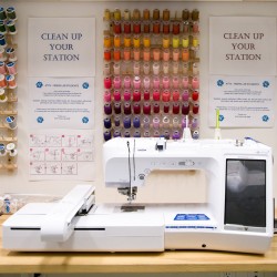 A photograph of a Brother digital embroidery machine in front of 3 racks of spools of embroidery thread in a wide array of colors.