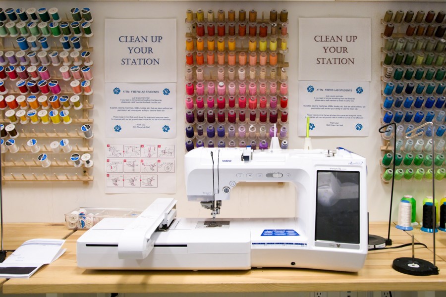 A photograph of a Brother digital embroidery machine in front of 3 racks of spools of embroidery thread in a wide array of colors.