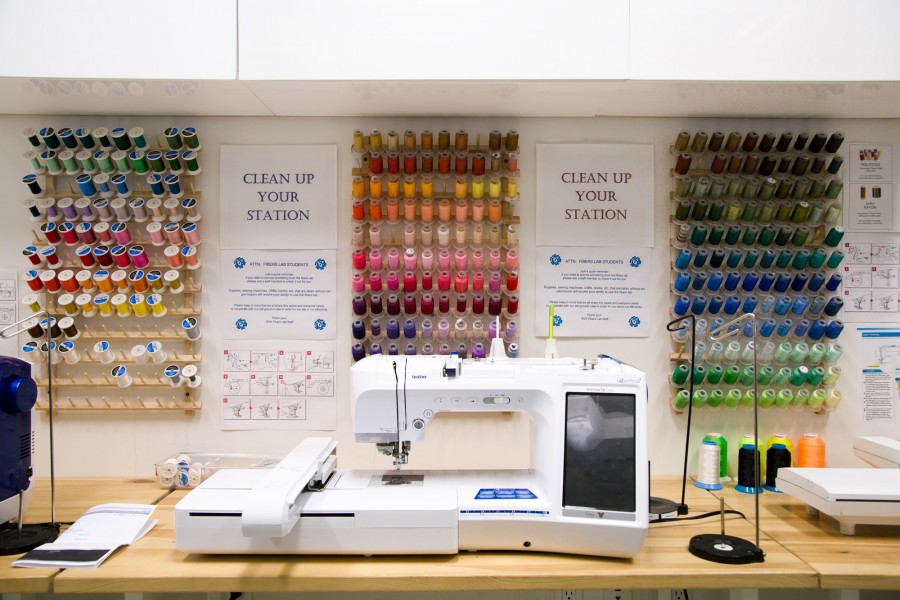 A Brother digital embroidery machine in front of three racks of embroidery thread in many different colors.