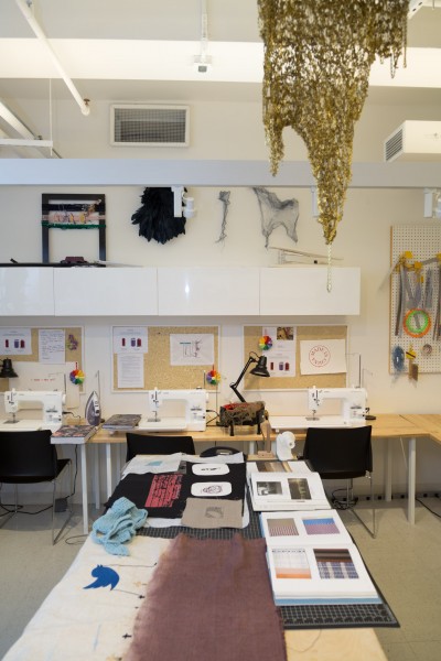 Overview of the fibers lab with a table which has fabric material on it, material catalogs and sewing machines in the background.