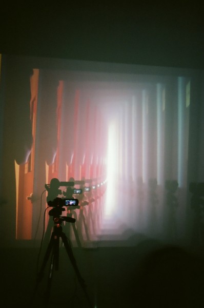 An image projected on the wall of an image inside an image going on to the infinite, and in front of the wall with the projection is a tripod with a small camcorder turned on