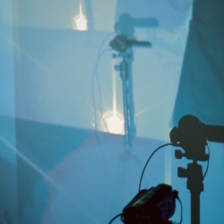An image projected on the wall of a mirror casts a shadow of a small video camera installed on a tripod in the lower right corner
