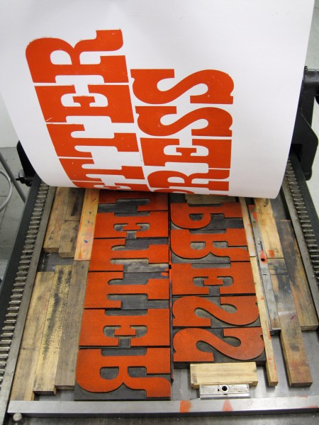Pulling off a letterpress print. The word "letterpress" is printed in red ink on white paper.
