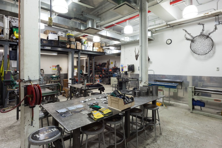 Safety equipments and sanding materials on the front table. Forming machines and Stationary sanding machine on the back. Student's metal works are on the wall.