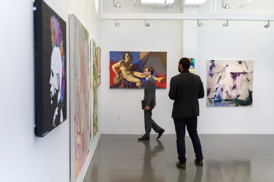 Installation view of several paintings with two persons looking at one painting.