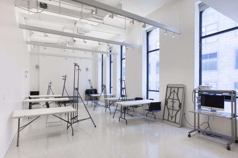 One of the painting classrooms in the BFA fine Arts building at the School of Visual Arts. The room is filled with white tables and metal painting easels. There are windows on the right side of the room.